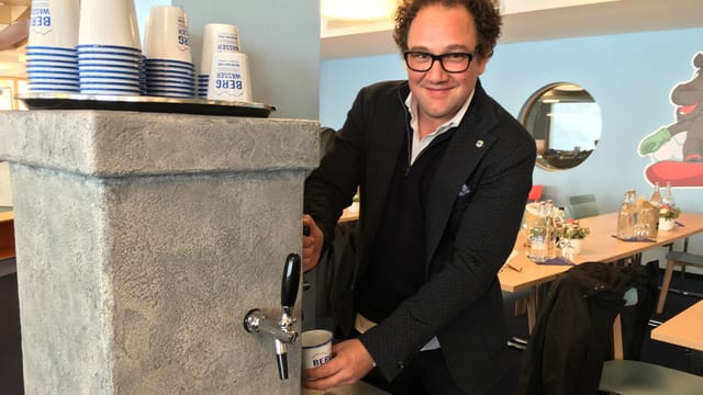Ein Mann, welcher an einem Brunnen einen Becher mit Wasser füllt. Ein Mann, welcher an einem Brunnen einen Becher mit Wasser füllt.