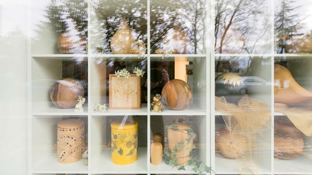 Ein Schaufenster mit Holzurnen, in dem sich Bäume spiegeln. Ein Schaufenster mit Holzurnen, in dem sich Bäume spiegeln.
