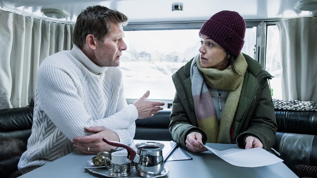 Ein Frau und ein Mann sprechen miteinander in einem Wohnwagen. Sie trägt Winterkleidung mit Wollmütze und hlät ein Papier in der Hand, Ein Frau und ein Mann sprechen miteinander in einem Wohnwagen. Sie trägt Winterkleidung mit Wollmütze und hlät ein Papier in der Hand,