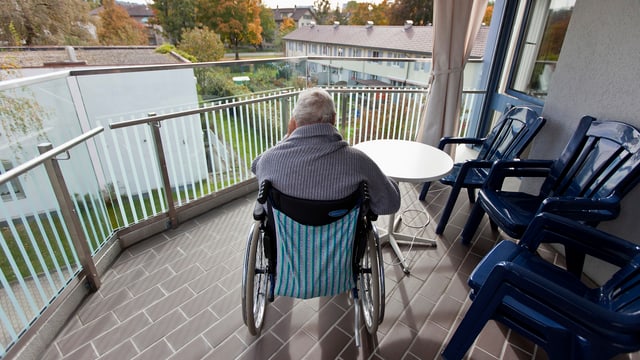 Eine Person sitzt auf dem Balkon im Rollstuhl Eine Person sitzt auf dem Balkon im Rollstuhl