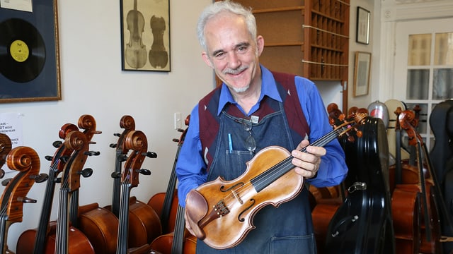 Roland Feller mit einer Geige in den Händen. Im Hintergrund Celli. Roland Feller mit einer Geige in den Händen. Im Hintergrund Celli.