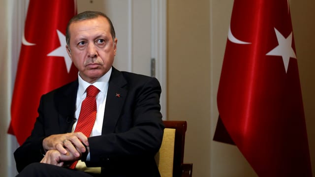 Erdogan sitzt vor türkischen Flaggen.