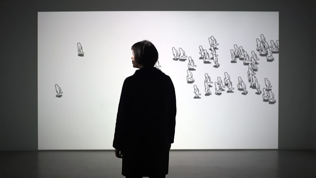 Eine Person steht vor einer Leinwand, auf der gezeichnete Figuren herumrennen. Eine Person steht vor einer Leinwand, auf der gezeichnete Figuren herumrennen.