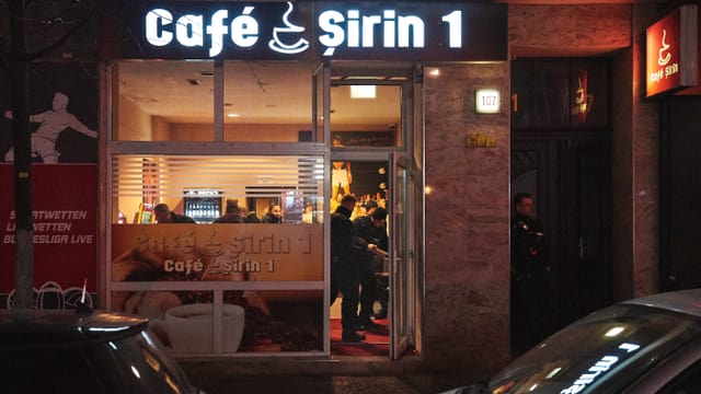 Ein Café von Aussen. Man sieht wie Drinnen Polizisten stehen. Ein Café von Aussen. Man sieht wie Drinnen Polizisten stehen.
