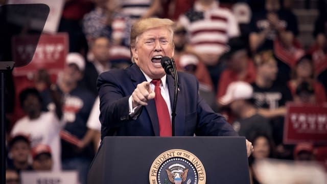 Trump spricht auf einem Podest und gestikuliert. Trump spricht auf einem Podest und gestikuliert.