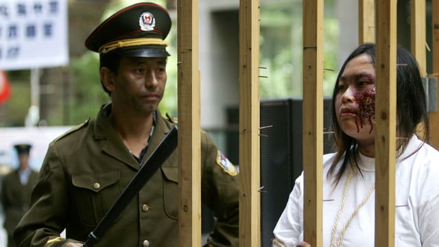 Falung-Gong-Anhänger in falscher Polizeiuniform (links) bewacht eine als Gefangene verkleidete Frau. Falung-Gong-Anhänger in falscher Polizeiuniform (links) bewacht eine als Gefangene verkleidete Frau.
