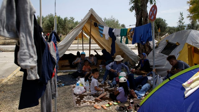 Menschen sitzen vor einem Zelt in einem Flüchtlingslager in Mytilene.