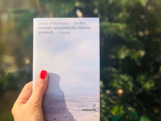 Das Buch Usama Al Shahmani: «In der Fremde sprechen die Bäume arabisch» vor einem Weihnachtsbaum Das Buch Usama Al Shahmani: «In der Fremde sprechen die Bäume arabisch» vor einem Weihnachtsbaum