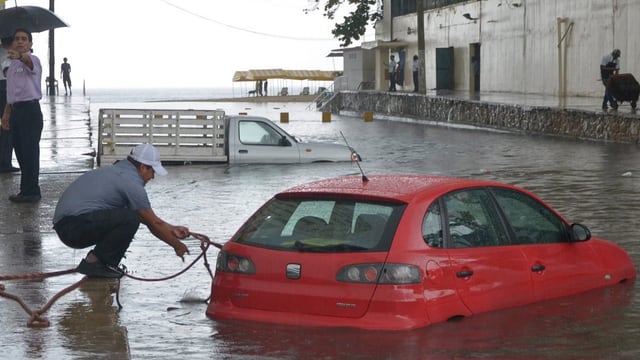 Ein Mann versucht ein Sicherungsseil an einem Auto im Wasser anzubringen. Ein Mann versucht ein Sicherungsseil an einem Auto im Wasser anzubringen.