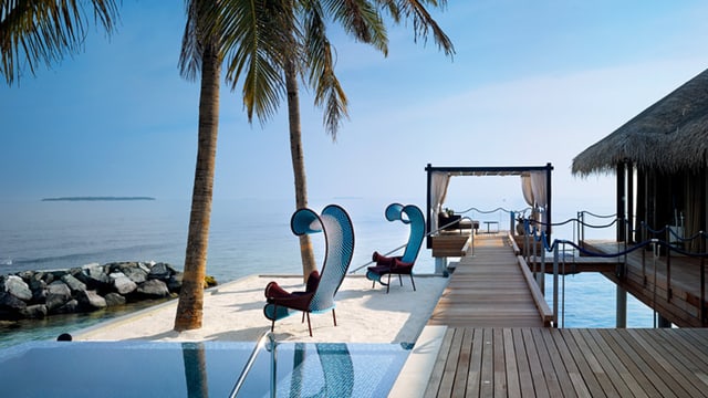 Ein Pool mit futuristische Liegestühlen und einem Bungalow mit Sicht aufs Meer. Ein Pool mit futuristische Liegestühlen und einem Bungalow mit Sicht aufs Meer.