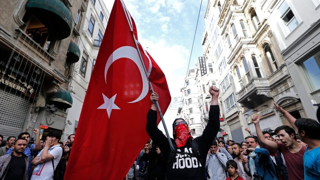 Ein vermummter Demonstrant hält eine türkische Flagge hoch.