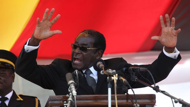 Mugabe an einem Rednerpult, hinter ihm eine Flagge. Mugabe an einem Rednerpult, hinter ihm eine Flagge.