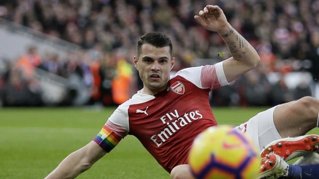 Ein Fussballer schliddert auf nassem Boden dem Ball entgegen. Am Arm ein Binde in Regenbogenfarben. Ein Fussballer schliddert auf nassem Boden dem Ball entgegen. Am Arm ein Binde in Regenbogenfarben.