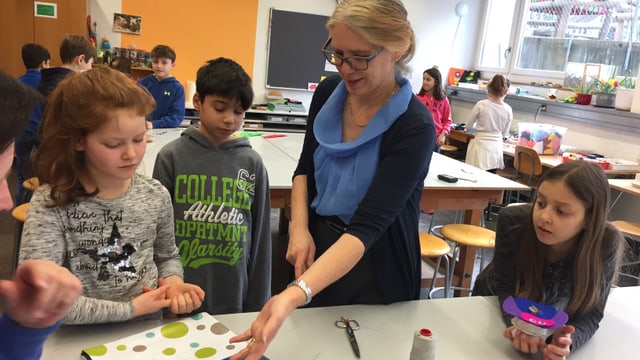 Eien Lehrerin in einem Schulzimmer zeigt drei Schülern, was sie machen sollen. Eien Lehrerin in einem Schulzimmer zeigt drei Schülern, was sie machen sollen.
