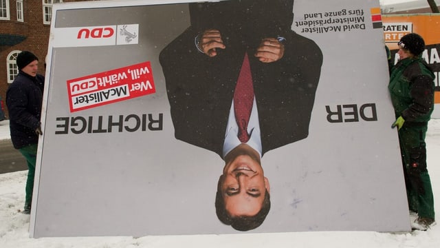 Zwei Menschen demontieren ein Plakat von David McAllister. Zwei Menschen demontieren ein Plakat von David McAllister.