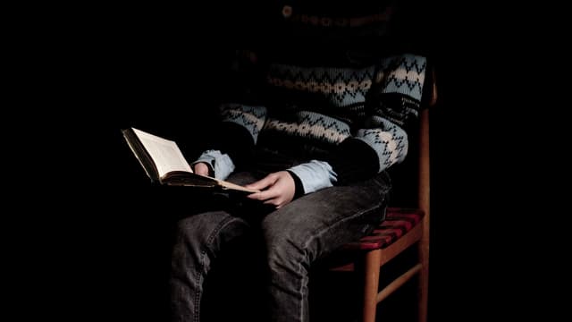 Ein Junge liest ein Buch, das Gesicht ist verdunkelt.