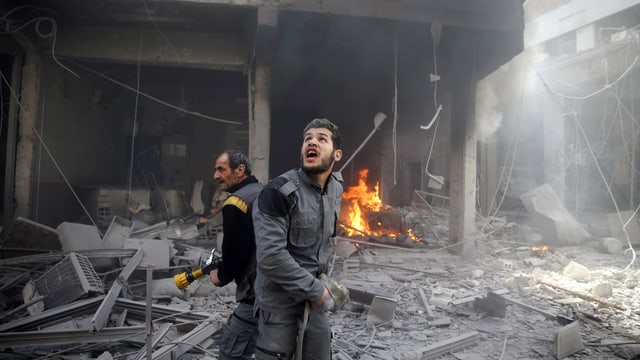 Zwei Helfer versuchen in zerbombten Häusern Feuer zu löschen. Zwei Helfer versuchen in zerbombten Häusern Feuer zu löschen.