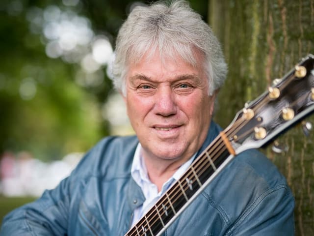 Mann mit grauen Haaren und Gitarre in der Hand steht vor Baum. Mann mit grauen Haaren und Gitarre in der Hand steht vor Baum.