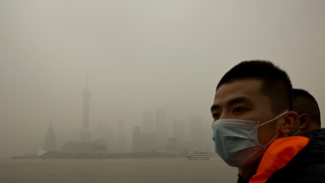 Ein Mann mit Gesichtsmaske vor der Smog-verhangenen Skyline von Schanghai. Ein Mann mit Gesichtsmaske vor der Smog-verhangenen Skyline von Schanghai.