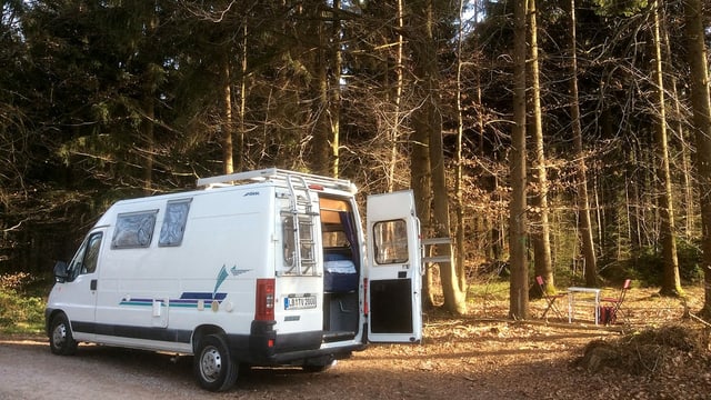 Ein Fiat Ducato Bus im Wald. Daben steht ein Campingtisch und 2 Stühle. Ein Fiat Ducato Bus im Wald. Daben steht ein Campingtisch und 2 Stühle.