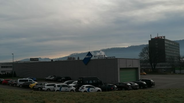 Eine niedrige Halle, umstellt von Autos, rechts daneben ein grösseres Gebäude. Eine niedrige Halle, umstellt von Autos, rechts daneben ein grösseres Gebäude.