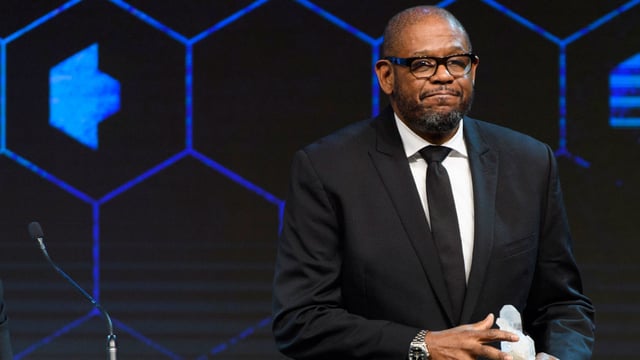 Schauspieler Forest Whitaker mit zusammengekniffenen Lippen und einem Preis in der Hand. Schauspieler Forest Whitaker mit zusammengekniffenen Lippen und einem Preis in der Hand.