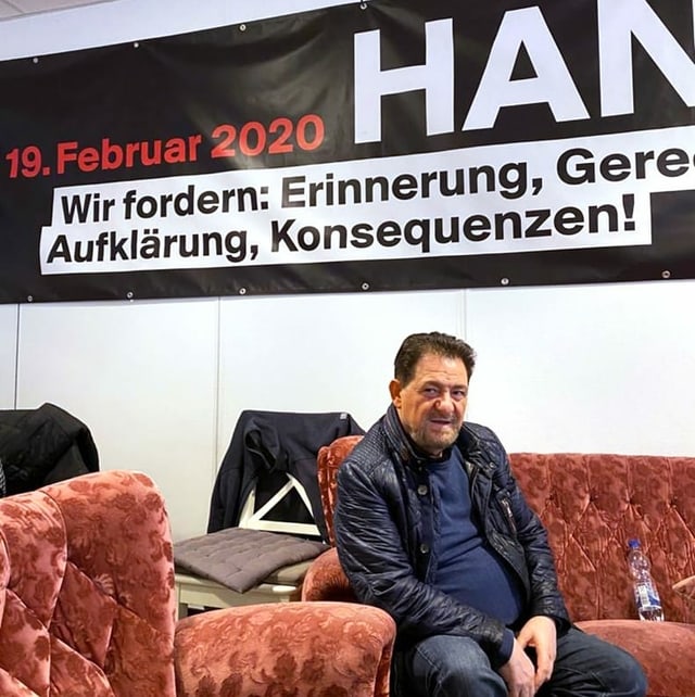 ein Mann sitzt auf einem Sofa, im Hintergrund ein Banner ein Mann sitzt auf einem Sofa, im Hintergrund ein Banner
