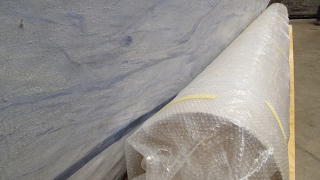 Grosses gerolltes Gemälde, das in Plastik eingepackt auf dem Boden liegt. Grosses gerolltes Gemälde, das in Plastik eingepackt auf dem Boden liegt.