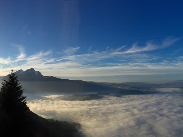 Blauer Himmel, am Horizont Schleierwolken. Im Vordergrund Nebelmeer mit einem Berg, der herausragt.