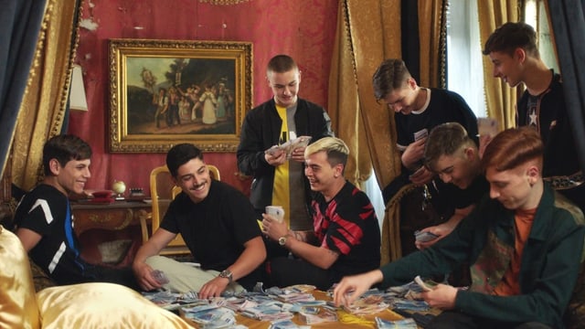 Nicola und seine Bande zählen und sortieren lachend Geld auf einem Bett. Nicola und seine Bande zählen und sortieren lachend Geld auf einem Bett.