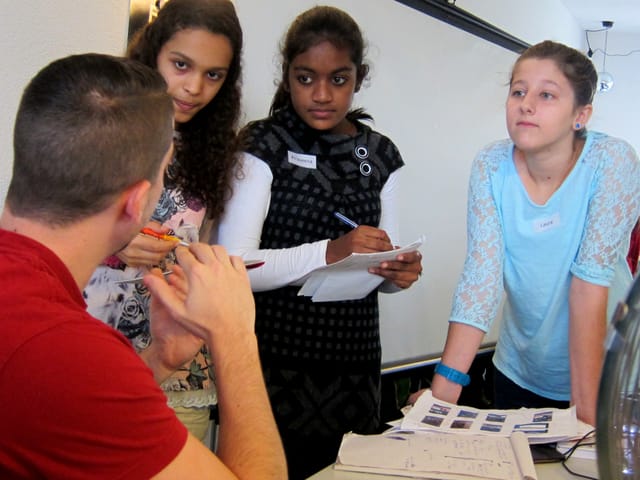 Drei Mädchen hören zu wie ein junger Mann ihnen etwas erzählt