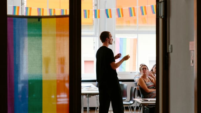 Ein Mann steht in einem Workshop-Raum voller Regenbogenflaggen. Ein Mann steht in einem Workshop-Raum voller Regenbogenflaggen.