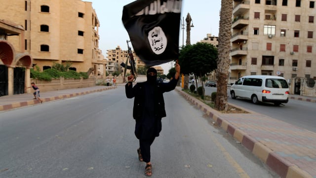 Ein IS-Kämpfer zieht mit erhobenem Gewehr und IS-Fahne in der Hand durch die Strassen Raqqas. Ein IS-Kämpfer zieht mit erhobenem Gewehr und IS-Fahne in der Hand durch die Strassen Raqqas.
