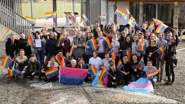 Eine Gruppe junger Menschen mit Regenbogenfahnen auf einem Kopfsteinpflasterplatz Eine Gruppe junger Menschen mit Regenbogenfahnen auf einem Kopfsteinpflasterplatz