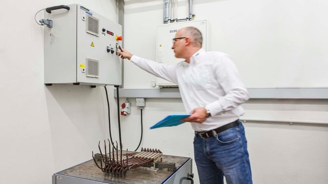 Mann dreht an Knopf einer Maschine, darunter Kabel auf einem Tisch Mann dreht an Knopf einer Maschine, darunter Kabel auf einem Tisch