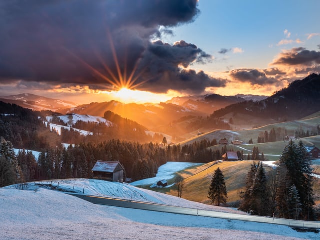 Sonnenuntergang über einer leicht verschneiten Hügellandschaft bei wechselnder Bewölkung. Sonnenuntergang über einer leicht verschneiten Hügellandschaft bei wechselnder Bewölkung.