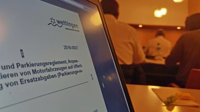 Computer-Bildschirm mit Einwohnerratsvorlage zu Parkierungsreglement, im Hintergrund Parlamentarier im Plenarsaal. Computer-Bildschirm mit Einwohnerratsvorlage zu Parkierungsreglement, im Hintergrund Parlamentarier im Plenarsaal.