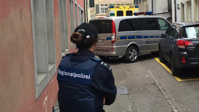 Polizistin steht vor Polizeifahrzeug in einer engen Gasse Polizistin steht vor Polizeifahrzeug in einer engen Gasse