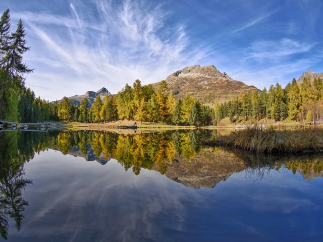 Bergsee mit farbigem Wald, blauem Himmel mit Cirren.