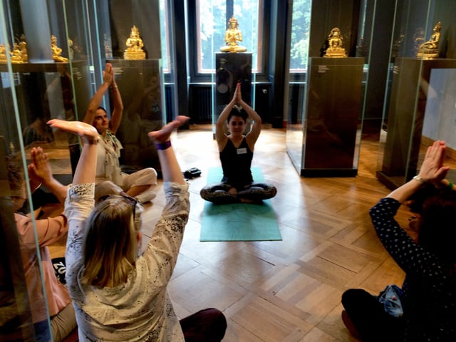 Visitors to a museum sit on the floor in the yoga lotus position.