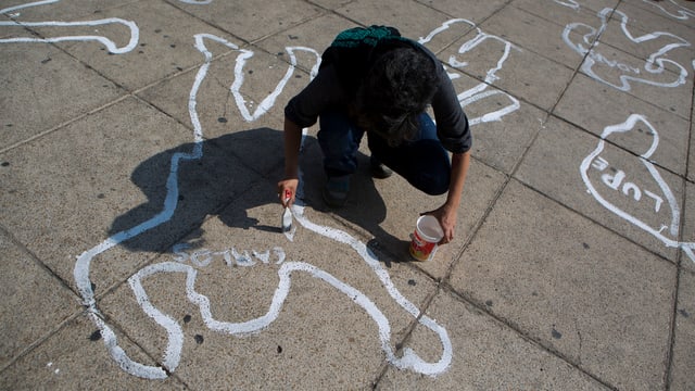 Eim Mann zeichnet die Umrisse von Leichen auf einen Platz.