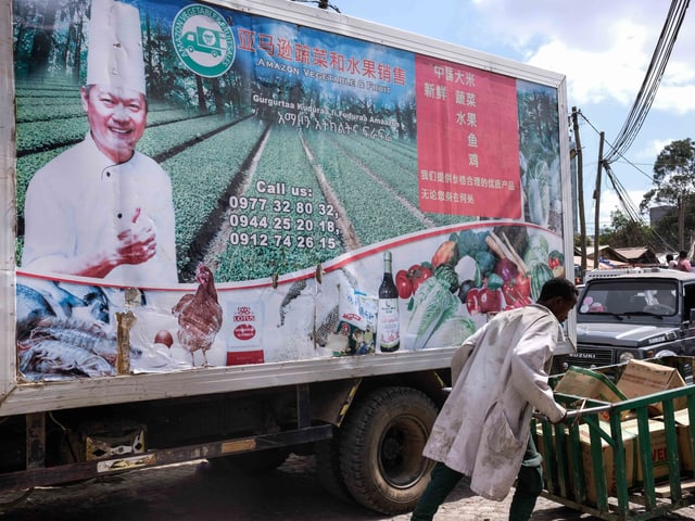 Ein Afrikaner schiebt seinen Handwagen vor einer chinesischen Werbung vorbei. Ein Afrikaner schiebt seinen Handwagen vor einer chinesischen Werbung vorbei.