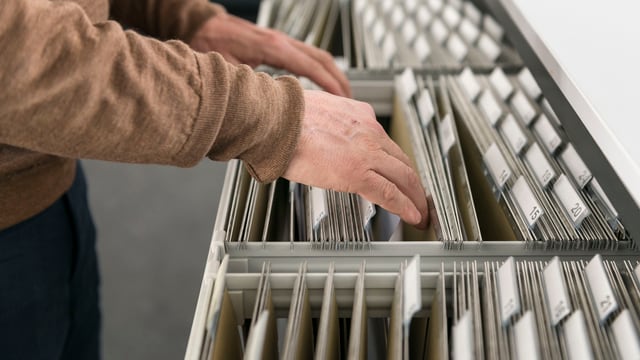 Eine Person sucht Akten in einem Aktenschrank. Eine Person sucht Akten in einem Aktenschrank.