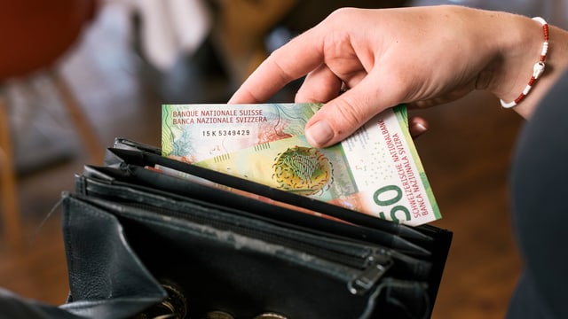 Hand, die eine Banknote in ein Portemonnaie legt. Hand, die eine Banknote in ein Portemonnaie legt.