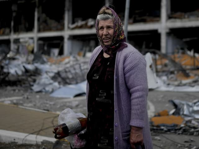 Eine alte Frau steht vor zerstörten Gebäuden.