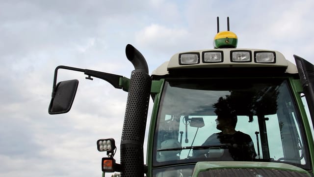 Ein Traktor, auf dem Dach ist eine grün-gelbe GPS-Box mit zwei Antennen montiert. Ein Traktor, auf dem Dach ist eine grün-gelbe GPS-Box mit zwei Antennen montiert.