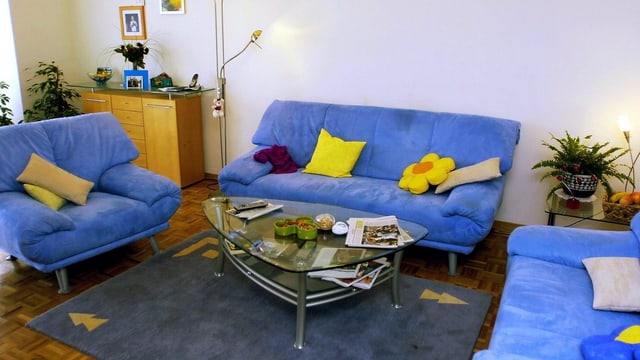 Wohnzimmer mit drei blauen Sofas, einem Teppich und einem Salontisch. Wohnzimmer mit drei blauen Sofas, einem Teppich und einem Salontisch.