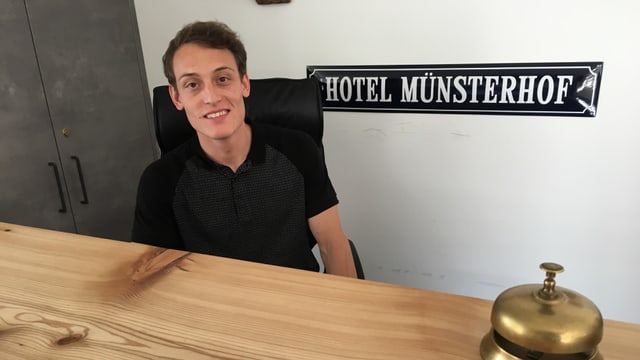 Junger Mann sitzt hinter Reception Junger Mann sitzt hinter Reception