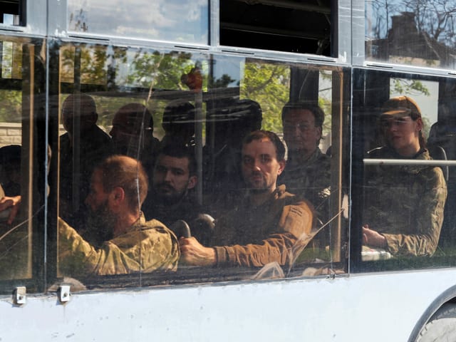 Ein Bus mit Angehörigen der ukrainischen Streitkräfte, die sich im belagerten Stahlwerk Asowstal ergeben haben, fährt unter Eskorte des prorussischen Militärs davo