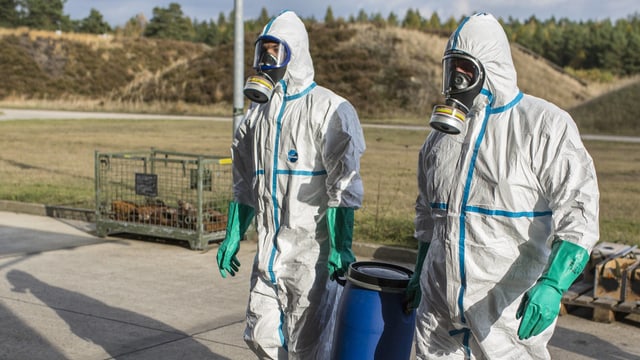 Symbolbild: Zwei Personen in Schutzanzügen und Gasmasken mit einem blauen Plastikfass. Symbolbild: Zwei Personen in Schutzanzügen und Gasmasken mit einem blauen Plastikfass.